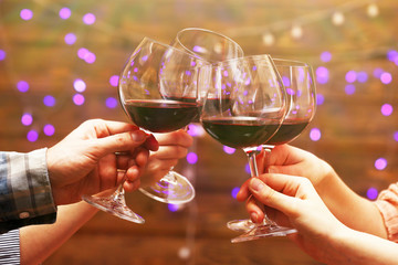Clinking glasses of red wine in hands on bright lights background