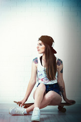 Fototapeta na wymiar Beautiful hipster girl with skateboard on light background