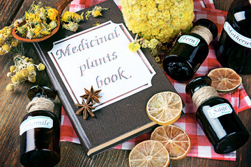 Medicinal plants book with dried herbs and bottles on table close up