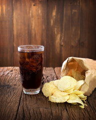 Cola and potato chips on wood background- junk food concept