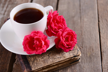 Old book with beautiful roses and cup of coffee on wooden table close up