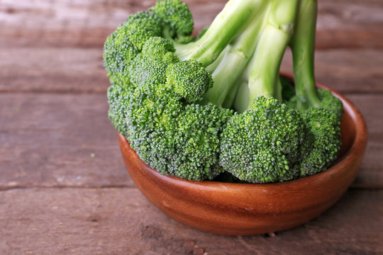 Fresh broccoli in bowl on wooden table close up