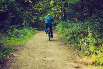 Vintage photo of man riding on bike through summertime forest