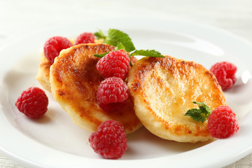 Fritters of cottage cheese with raspberries in plate on table, closeup