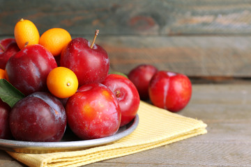 Ripe plums in metal plate on wooden background