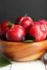 Ripe plums in bowl on wooden table on dark background