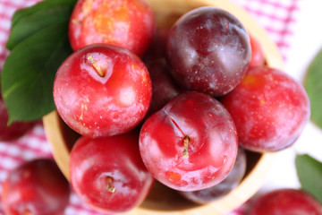 Ripe plums in bowl on wooden table with napkin, closeup