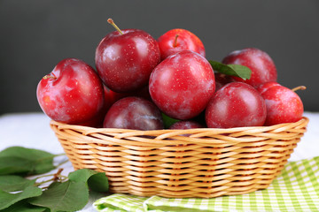 Ripe plums in wicker bowl on wooden table with napkin on dark background