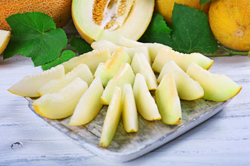 Slices of ripe melons with green leaves on table close up