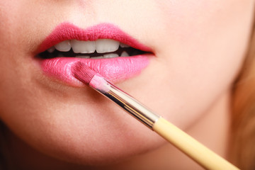 Naklejka premium Part of face. Woman applying pink lipstick with brush