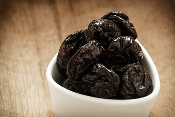 dried plums prunes in white bowl on wooden table