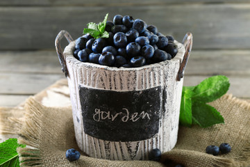 Tasty ripe blueberries with green leaves in bucket on table close up