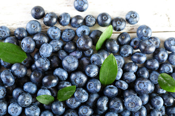 Tasty ripe blueberries with green leaves on wooden table close up