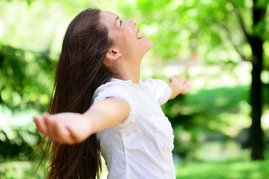 Joyful young woman with arms outstretched in park. Attractive mixed race Asian / Caucasian female is in casuals. She is looking up while smiling.