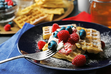 Sweet homemade waffles with forest berries and cream on plate, on dark wooden background