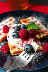 Sweet homemade waffles with forest berries and cream on plate, on dark wooden background