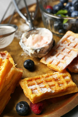Sweet homemade waffles and blueberries on tray, on color wooden background