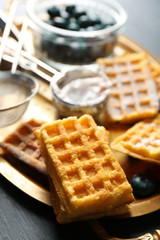 Sweet homemade waffles and blueberries on tray, on color wooden background