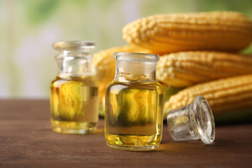 Fresh corn with bottles of oil on bright background
