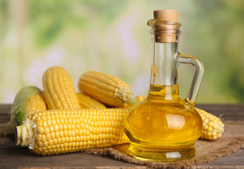 Bottle of oil with fresh corn on bright background