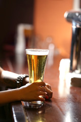 Fototapeta na wymiar Woman holding beer glass, close-up, on bar interior background