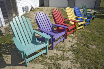 Fototapeta na wymiar Rainbow colored wooden chairs, known as Maine Chairs, standing in a row outside on the Eastern Shore, Maryland