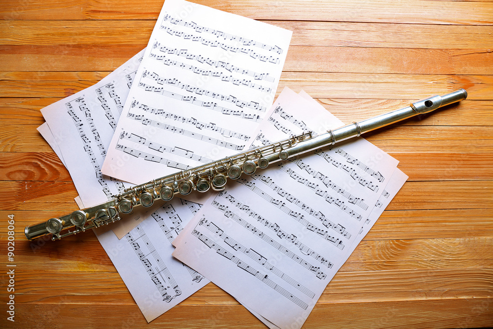 Wall mural Silver flute with music notes on wooden table close up