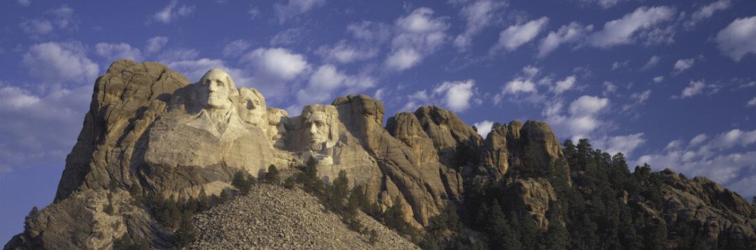Panoramic image with white puffy clouds behind Presidents George Washington, Thomas Jefferson, Teddy Roosevelt and Abraham Lincoln at Mount Rushmore National Memorial, South Dakota