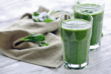 Glasses of spinach juice with napkin on wooden table, closeup