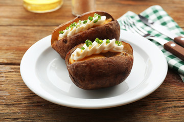 Baked potato mayonnaise and chives in white plate on wooden table, closeup