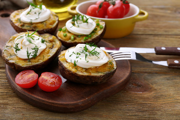 Baked potato with mayonnaise and herbs on wooden cutting board, closeup