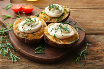 Baked potato with mayonnaise and herbs on wooden cutting board, closeup