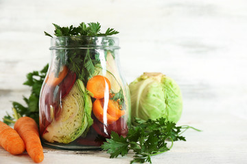 Fresh vegetables in glass bottle on wooden table on white wooden background