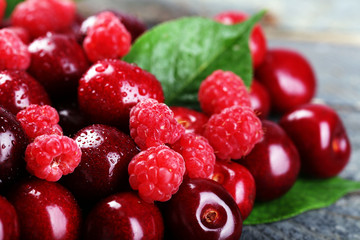 Sweet cherries, raspberries with green leaves on wooden background
