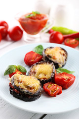Dish of eggplant with cherry tomatoes and cheese in white plate on wooden table, closeup