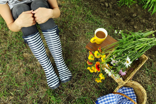 Young woman in rubber boots sitting on meadow outdoors