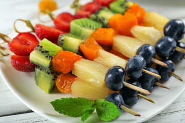 Fresh fruits on skewers in plate on wooden table, closeup