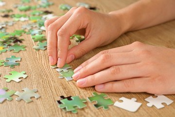 Female hands assembling puzzle on wooden table, closeup
