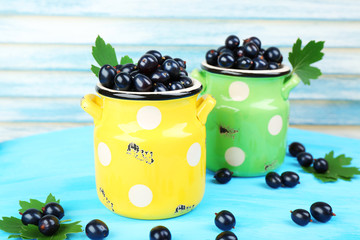 Ripe black currants in metal mugs on wooden background