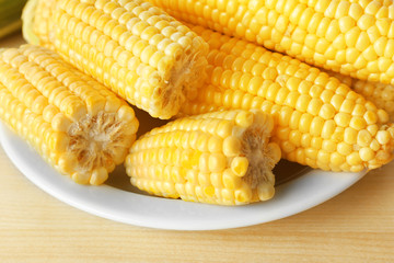 Fresh corn on cobs in plate on wooden table, closeup