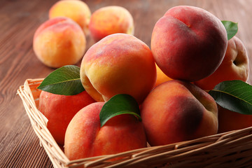 Fresh peaches in wicker basket on wooden table, closeup