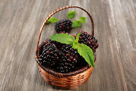 Ripe blackberries with green leaves in wicker basket on wooden background