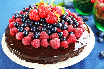 Delicious chocolate cake with summer berries on blue tablecloth, closeup