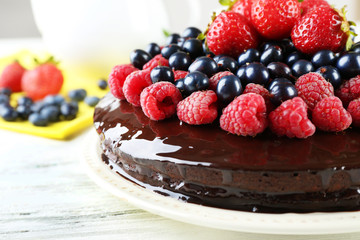 Delicious chocolate cake with summer berries on white wooden table, closeup