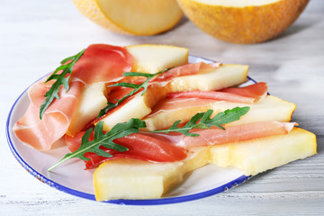 Melon with prosciutto of Parma ham on wooden table, closeup
