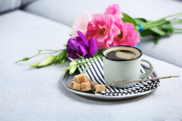 Cup of coffee with flowers on tray on sofa in room