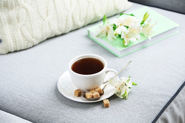 Fototapeta na wymiar Cup of coffee with lump sugar and flowers on sofa