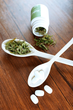 Dry medical cannabis and pills in spoons on table close up