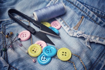 Colorful sewing buttons scissors and thread on jeans