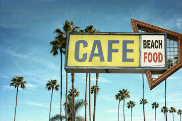 aged and worn vintage photo of cafe sign on beach with palm trees